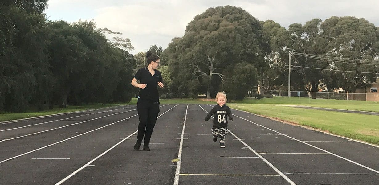 child running with educator on a track