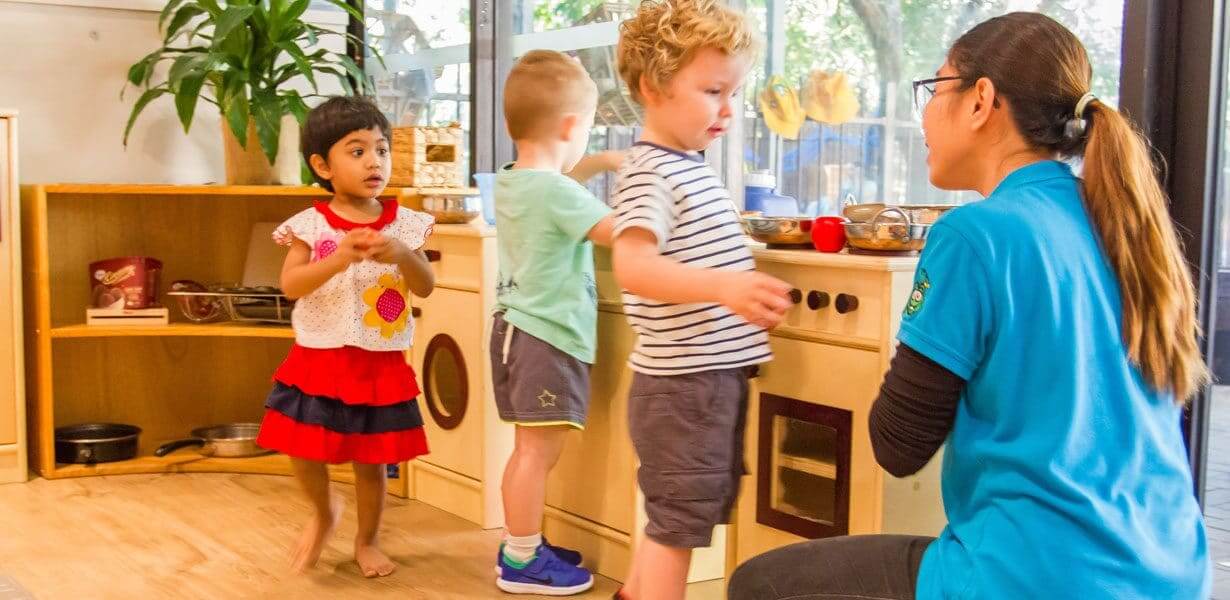 Three children and educator in front of play kitchen