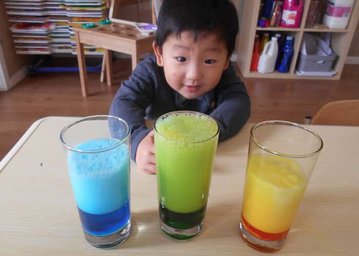 Child sitting with 3 different coloured glasses in front of him