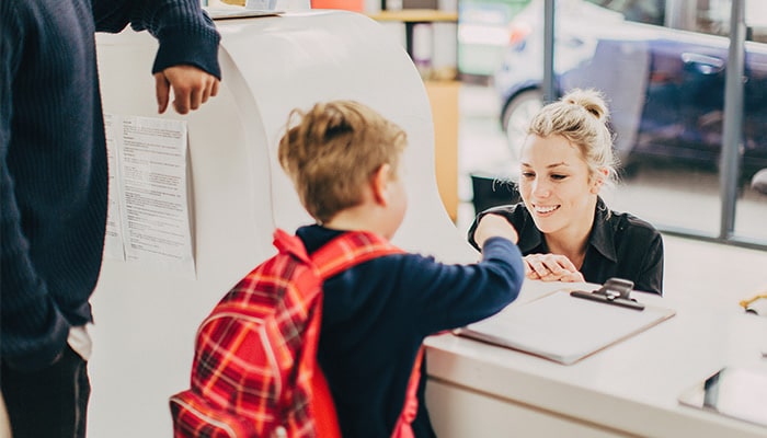 Child wearing backpack talking to educator at front desk