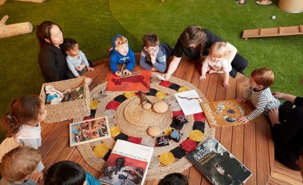 group of children and babies laying on a mat with books and toys, learning, sitting with Educators