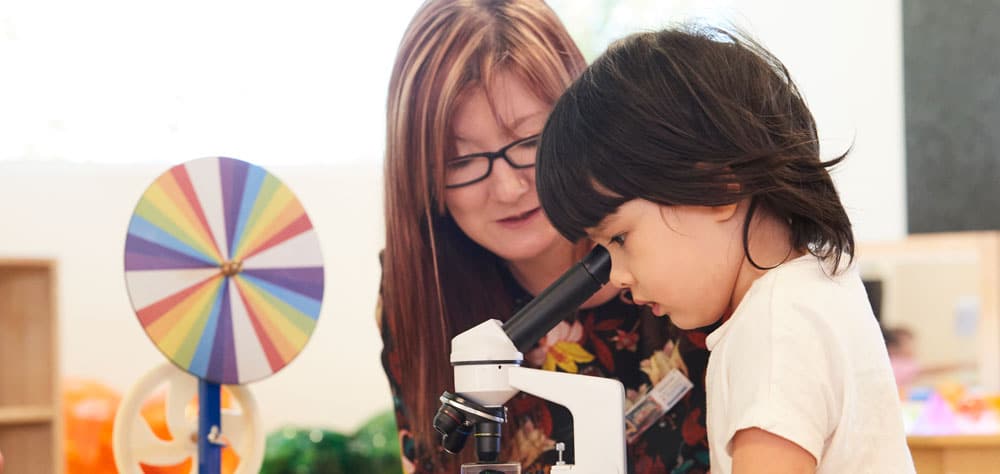 child with Educator looking through a microscope, curious, learning