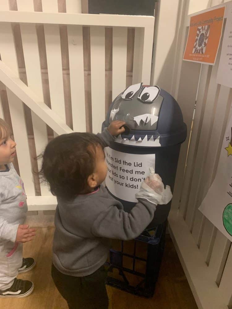 toddler adding plastic lids to Sid the Lid Monster bin