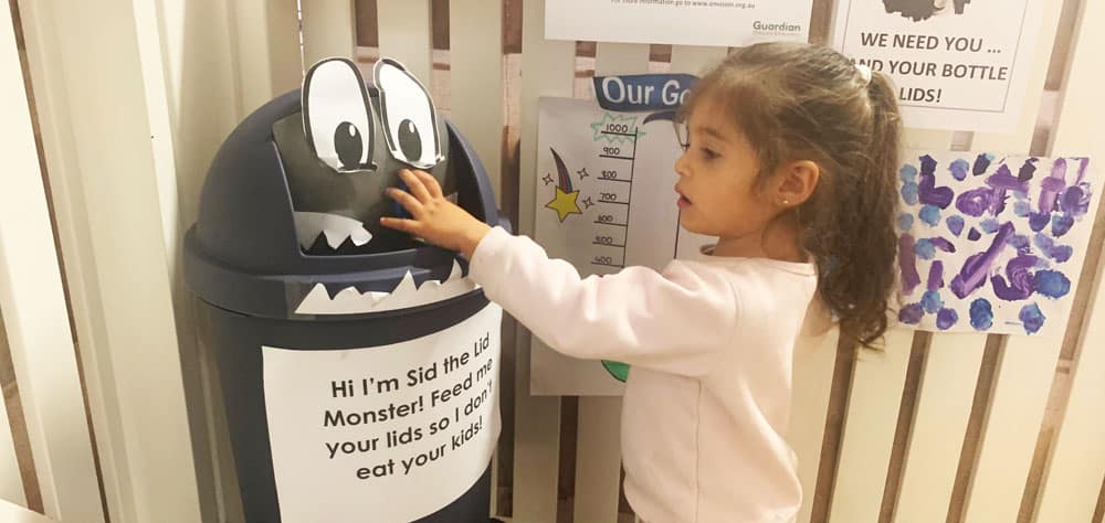child putting recycled lids into a decorated bin
