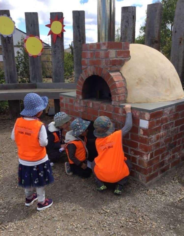 children wearing safety vests on an excursion looking at an outdoor pizza oven