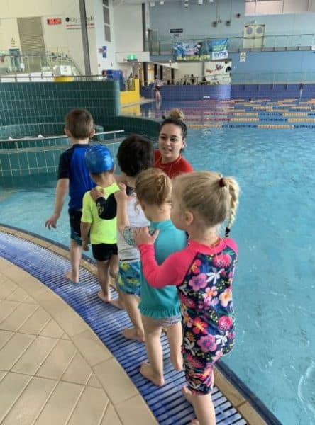 group of children at swimming lessons standing by pool with instructor