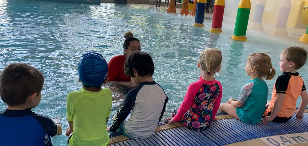 group of children sitting on edge of pool with instructor at swimming lessons