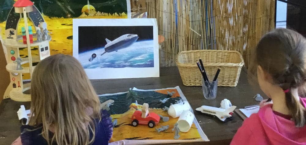 two children painting cars next to rocket ships and solar system display