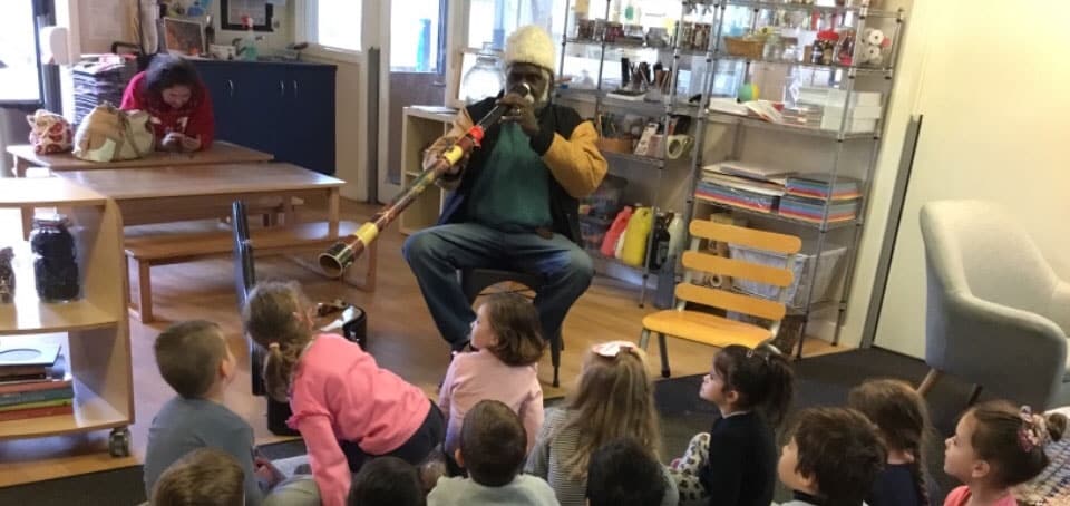 member of Aboriginal performance troupe plays didgeridoo to children