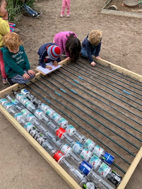 children outdoors building greenhouse out of plastic bottles