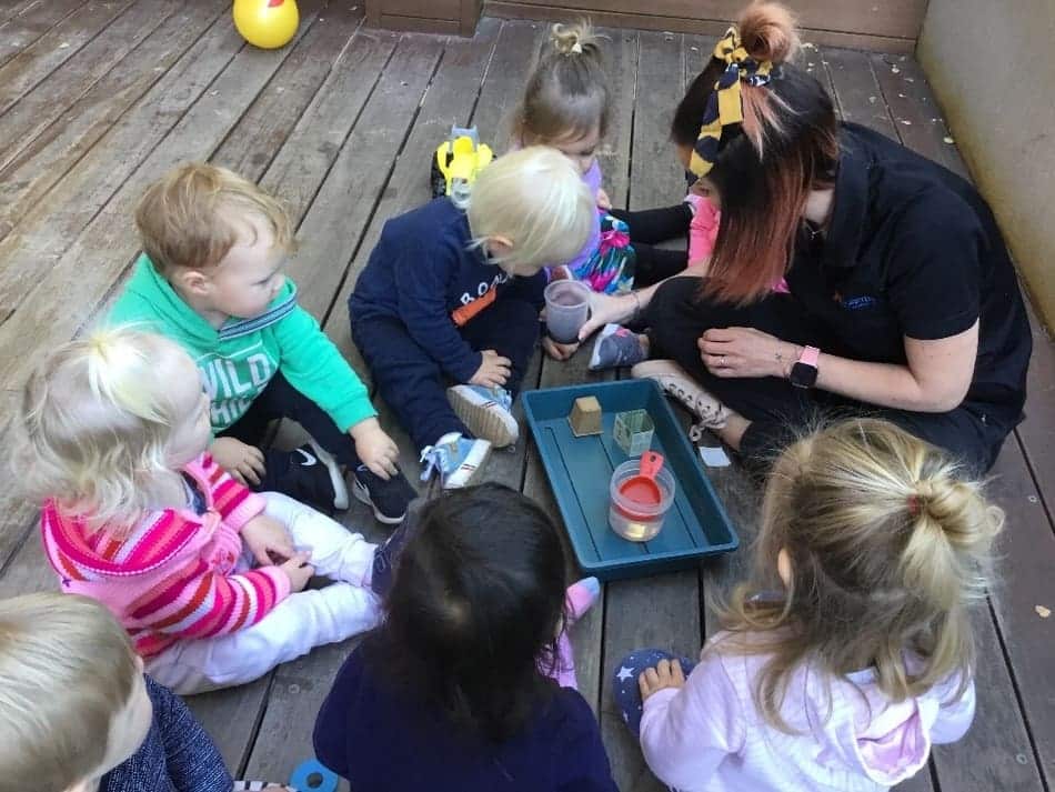 children sitting with Educator and looking at worms