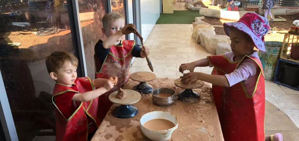 children in art smocks creating with clay