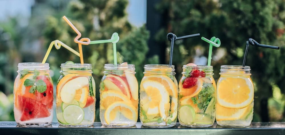 6 glass mason jars full of fruit and water and funky straws