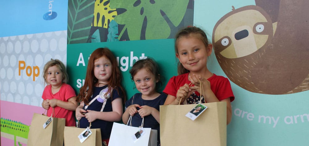 children holding care packages in front of Guardian mural