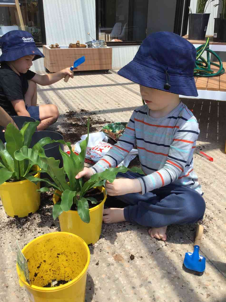 children wearing hats pot plants for neighbouring childcare centre