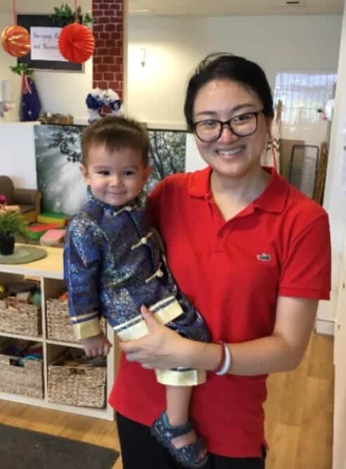 Educator wearing red shirt holding a child dressed in traditional Chinese costume