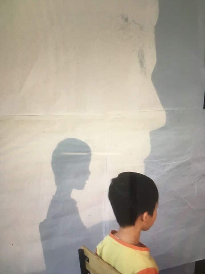 child sitting in front of projector to get his shadow traced during Summer Rain program