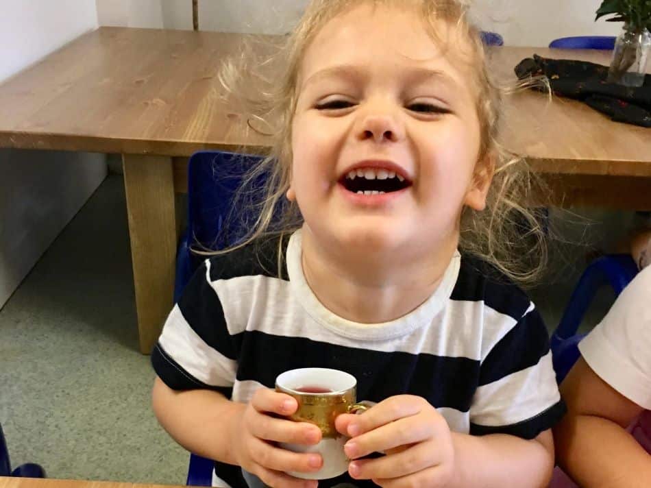 child laughing as she drinks tea during tea time