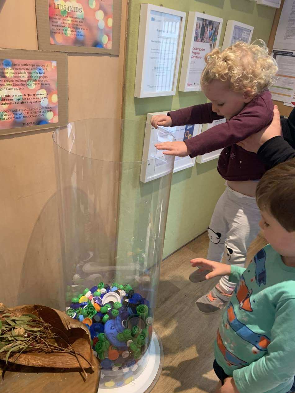 children dropping plastic lids into collection container