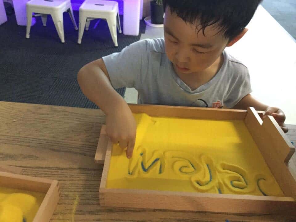 child learning to write his name in sand box