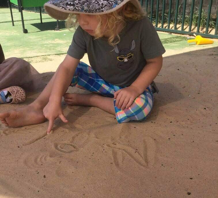 child learning to write his name in the sand