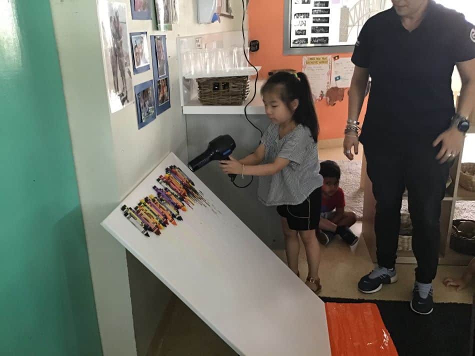 child holding hairdryer above crayons to melt them