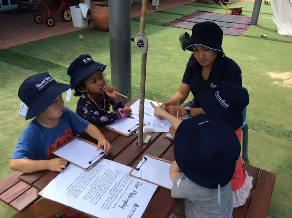 children sitting outside with Educator to review Centre philosophy