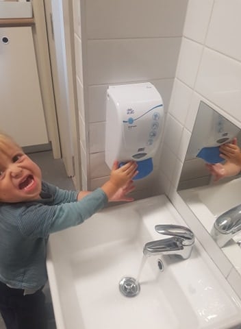 child using soap dispenser as part of hand washing routine