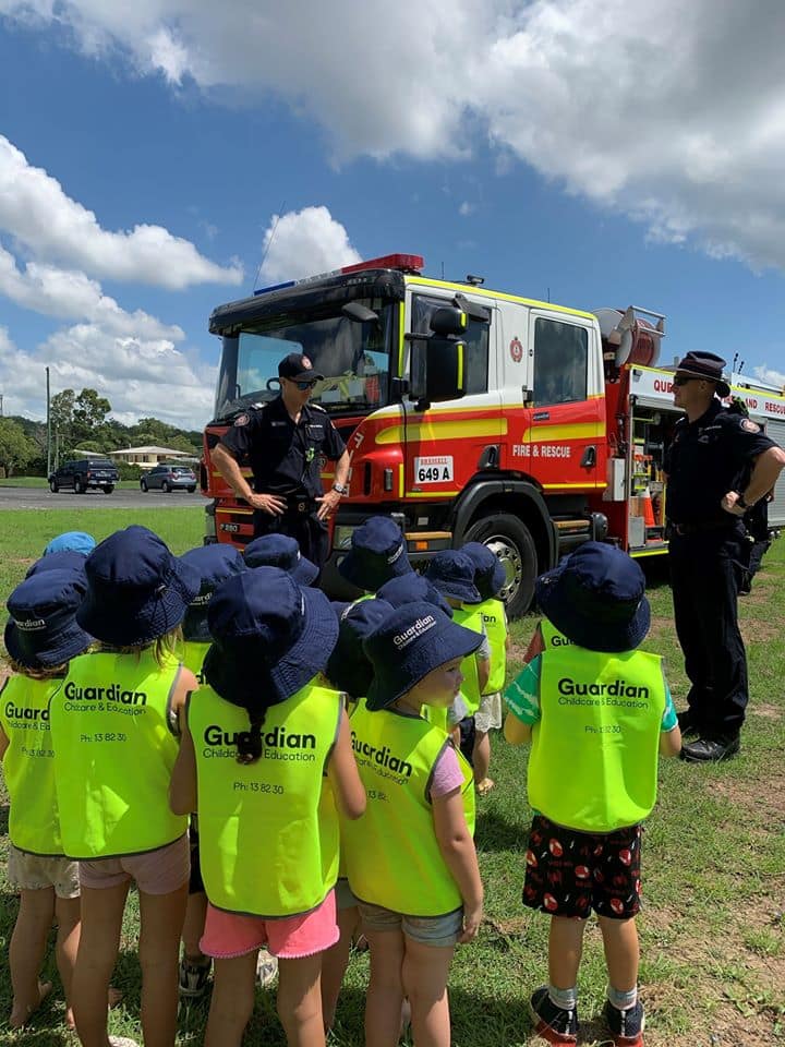 members of local fire brigade teaching children about fire truck