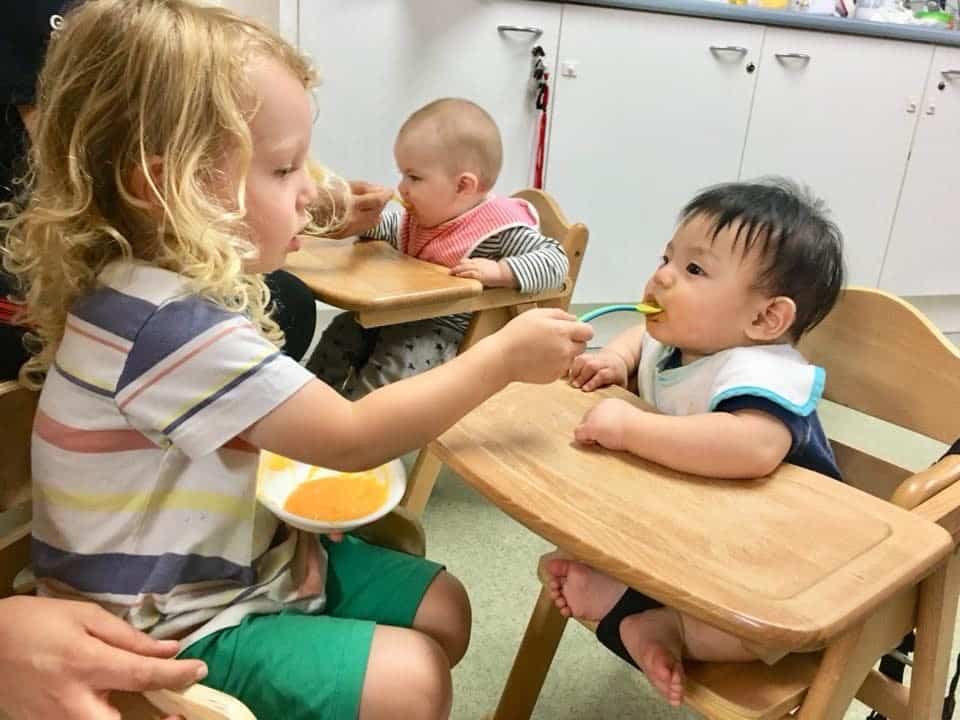 child feeding baby in highchair