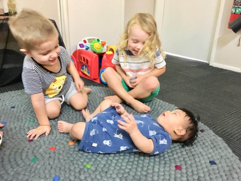 children laughing and playing with baby on mat