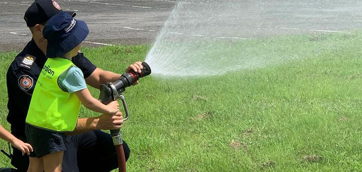 member of local fire brigade helping child hold fire truck hose