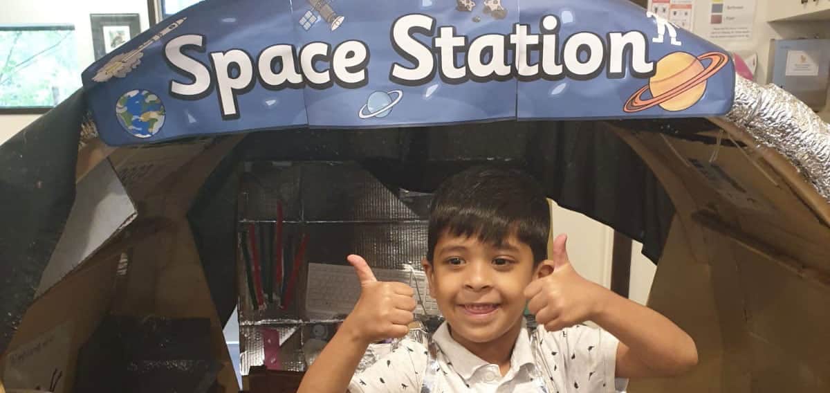 child with thumbs up and smiling in front of space station