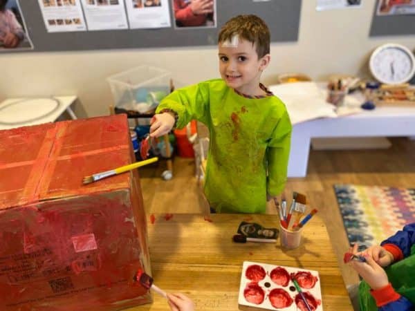 child wearing paint smock and painting cardboard mailbox