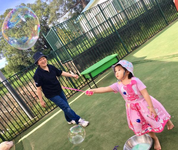 child and Educator outdoors playing with giant bubbles