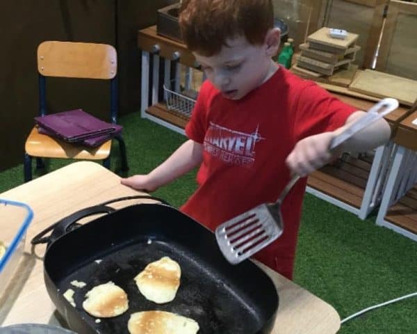 child holding spatula to flip pancakes during weekly cooking experiences