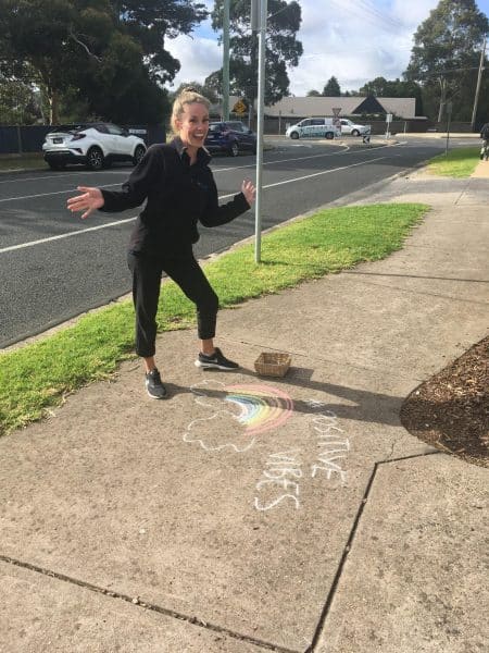 Educator smiling and standing next to chalk mural on footpath