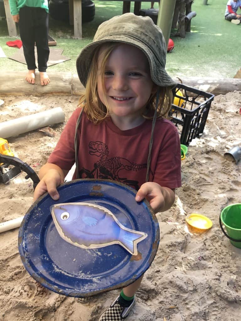 child wearing a hat and holding a plate with a plastic fish on it