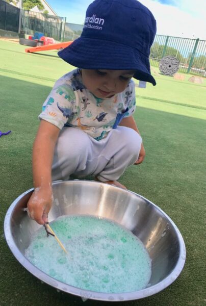 child sitting next to bowl of giant bubble mix