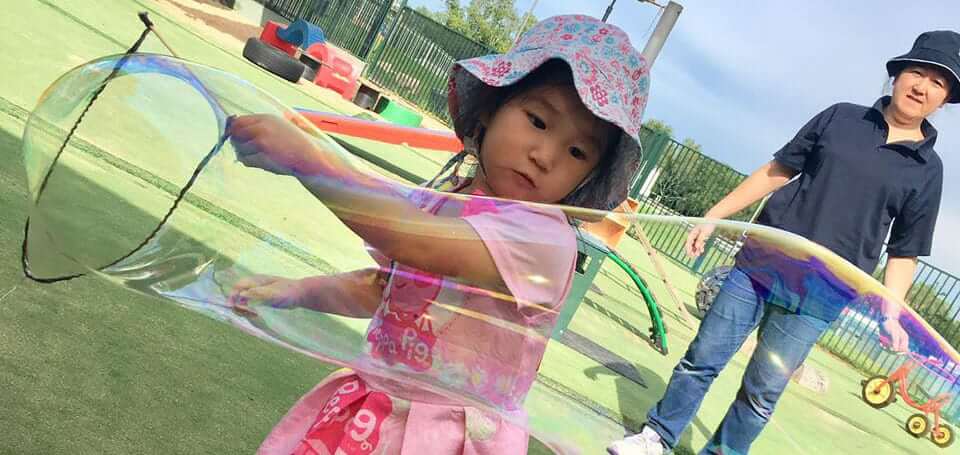 child @ Guardian Marsfield holding bubble wand, making giant bubble outdoors