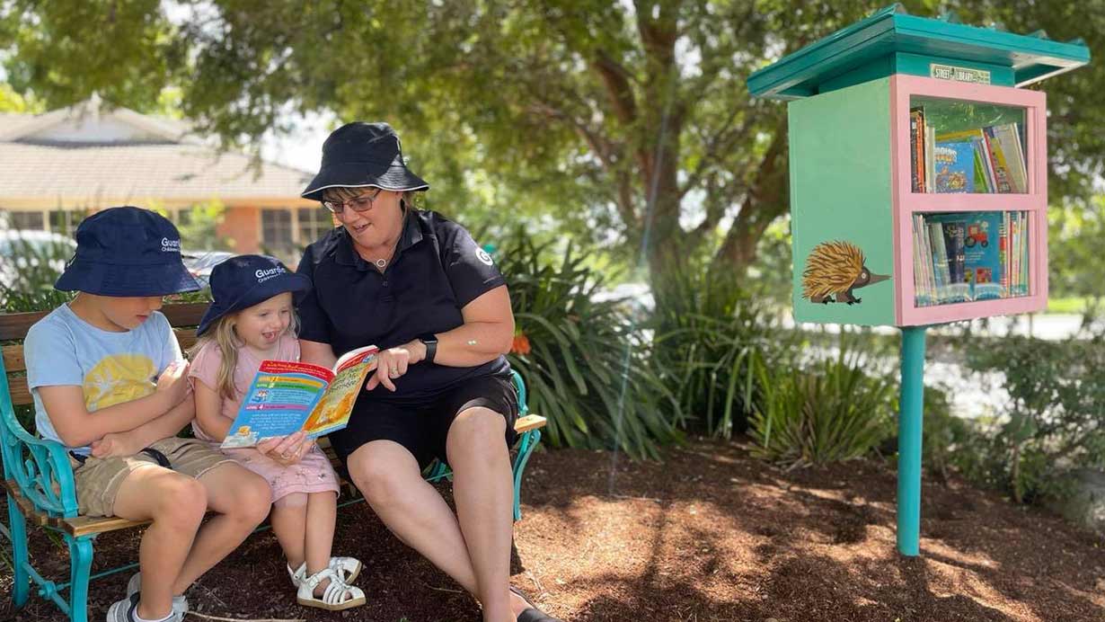 Children reading book with Educator near Street Library