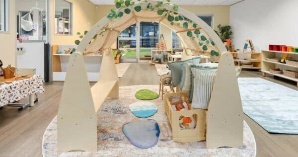 Inviting indoor play space at Guardian Childcare Barton featuring a wooden playhouse adorned with greenery, soft cushions, and natural stepping stones, designed for imaginative play and exploration.