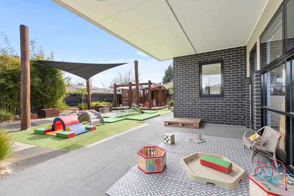 Sheltered outdoor patio at Guardian Childcare Point Cook West, featuring a soft play tunnel, slide, and activity centre on a patterned rug, providing protected play.