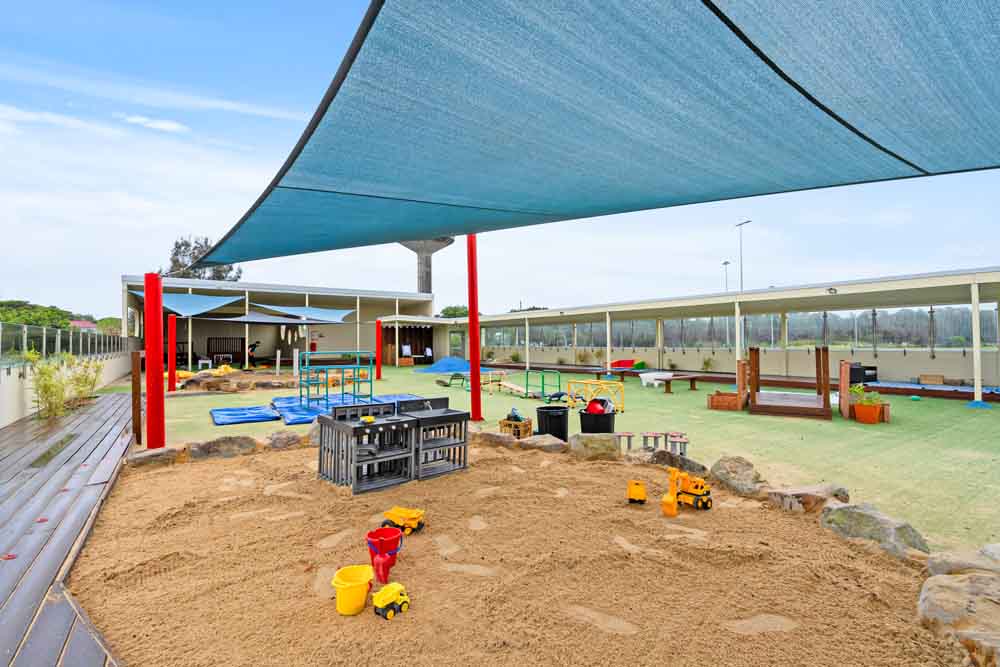 Sun-safe outdoor play area at Guardian Childcare Tempe, featuring a large sandpit, shade sail, water play table and diverse play equipment for active learning.